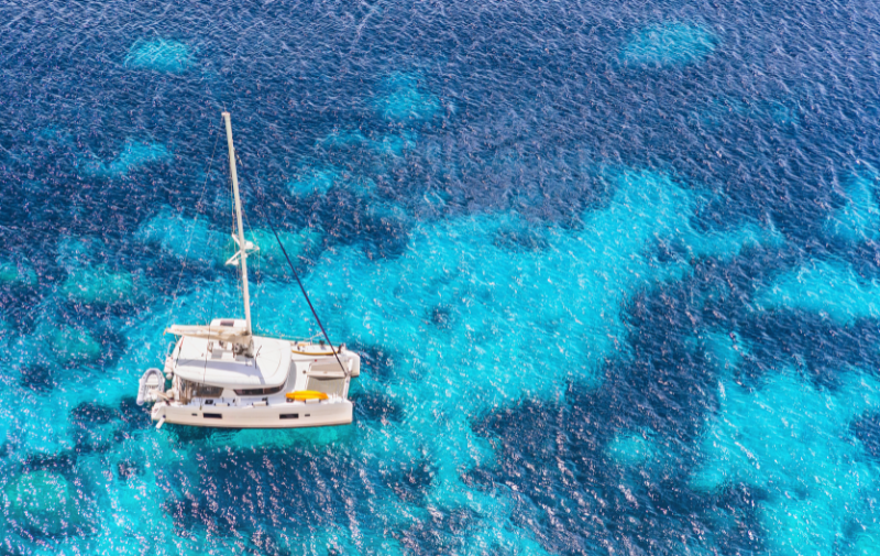 Ein eleganter Katamaran gleitet über tiefblaues, glasklares Meer. Die Sonne spiegelt sich auf der Wasseroberfläche, während das Boot vor einer weiten, fast endlosen Meereskulisse segelt – ein Sinnbild für moderne Segelcharter und den Trend zu komfortablen Katamaranreisen.